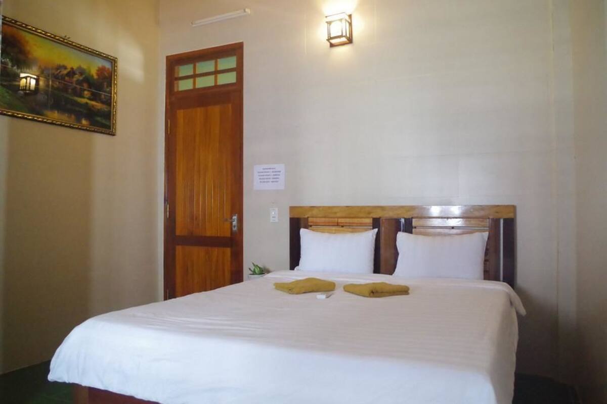 A hotel room with a wooden door, a bed with white bedding, and a painting on the wall.