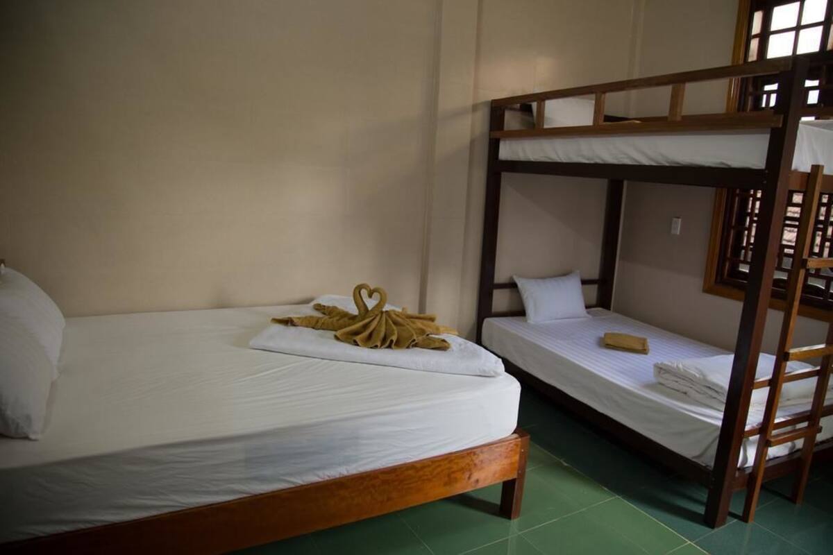 A room with two wooden bunk beds, one with a ladder, and a green tiled floor.