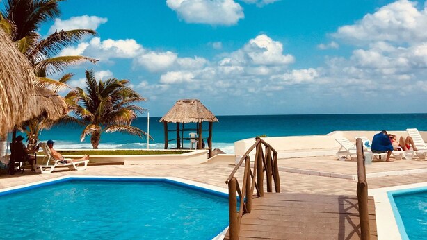 A pool area with a wooden deck, palm trees, and a thatched structure.