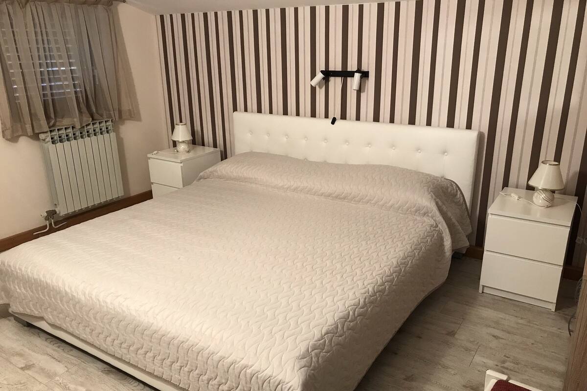 A bedroom with a large bed, two bedside tables, a radiator, and a striped wall.