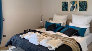 Una cama bien tendida con cubrecama acolchado, una lámpara de noche y una mesita de noche con toallas.