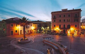 Una plaza con una fuente central, rodeada de edificios con terrazas al aire libre y letreros iluminados.