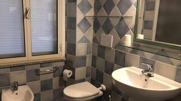 Un baño con bidé, inodoro y lavamanos, que presenta un diseño geométrico en las paredes.