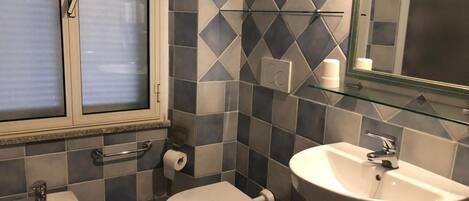 A bathroom with a bidet, toilet, and sink, featuring a geometric tile pattern on the walls.