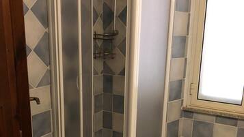 A bathroom with a shower enclosure, a sink, and a window.