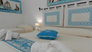 Un lit bien fait, avec un oreiller bleu et des serviettes enroulées, une lampe de chevet et un mur orné d’un tableau encadré.