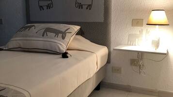 A bedroom with a bed, a headboard with animal illustrations, a bedside table with a lamp, and a wall-mounted switch.