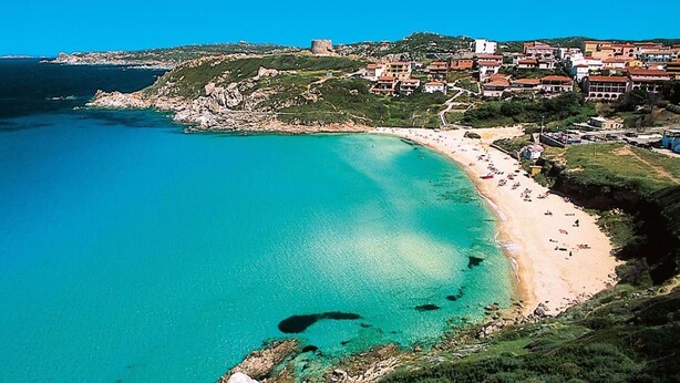 Une ville côtière dotée d’une plage de sable, d’eaux turquoise et limpides, et d’un château historique perché sur une colline.