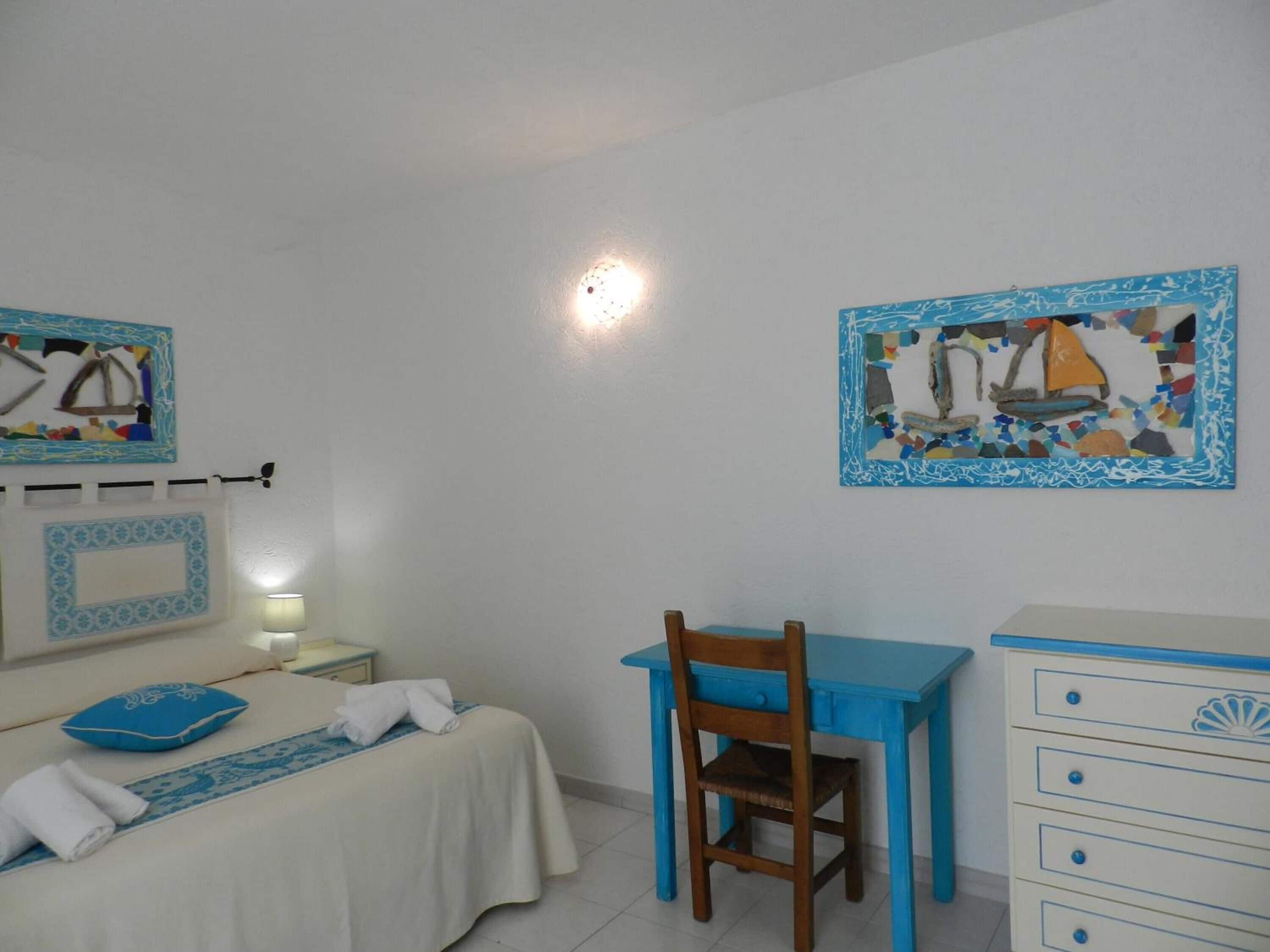 Een slaapkamer met een bed, een bureau en een stoel. Twee schilderijen hangen aan de muur.