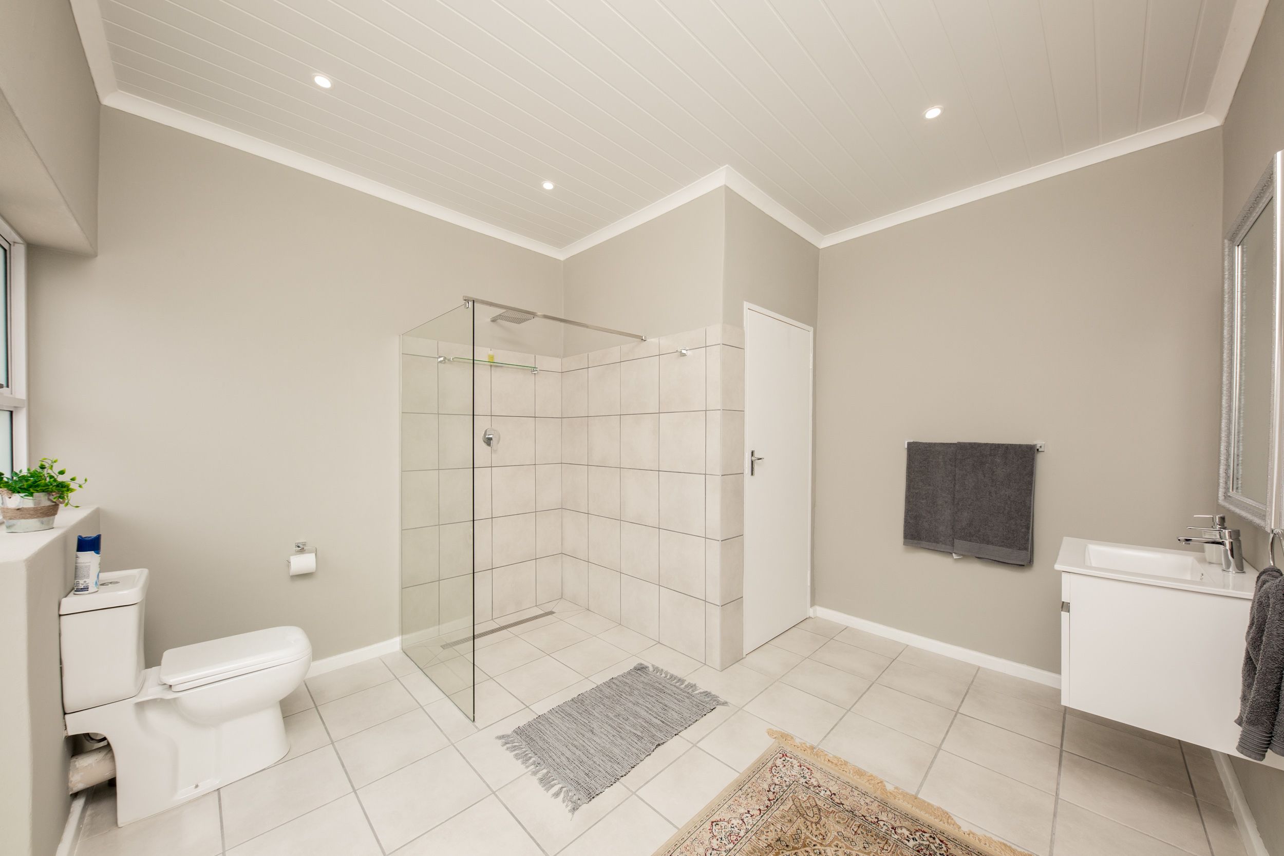 Een moderne badkamer met een douchecabine van glas, een toilet, een wastafel en een spiegel.