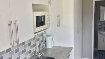 A modern kitchen with white cabinets, a stainless steel sink, a microwave, and a kettle.