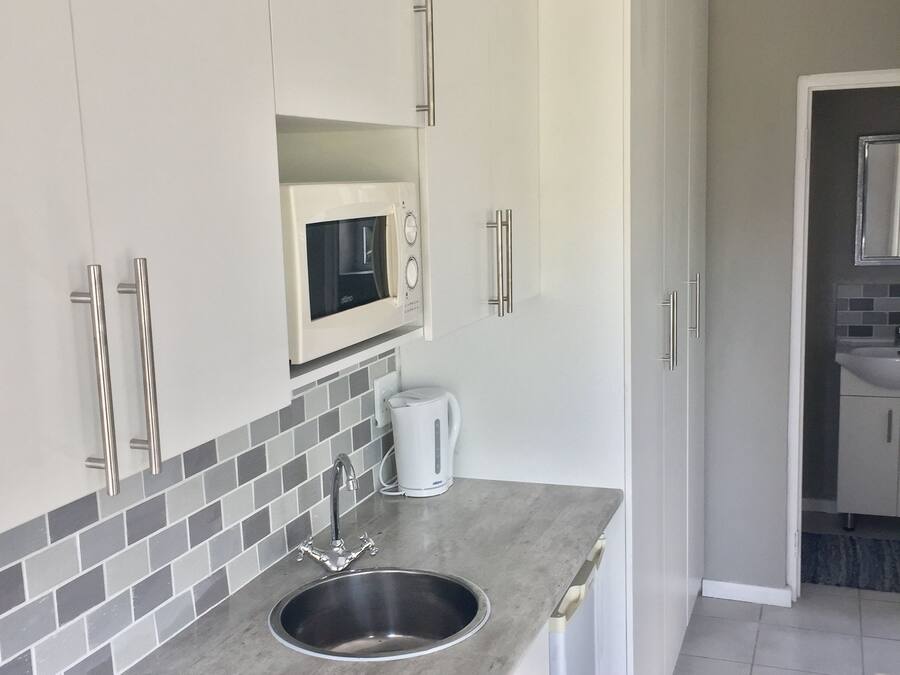 A modern kitchen with white cabinets, a stainless steel sink, a microwave, and a kettle.