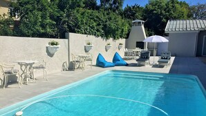 A swimming pool with lounge chairs and tables, surrounded by a white wall with planters.
