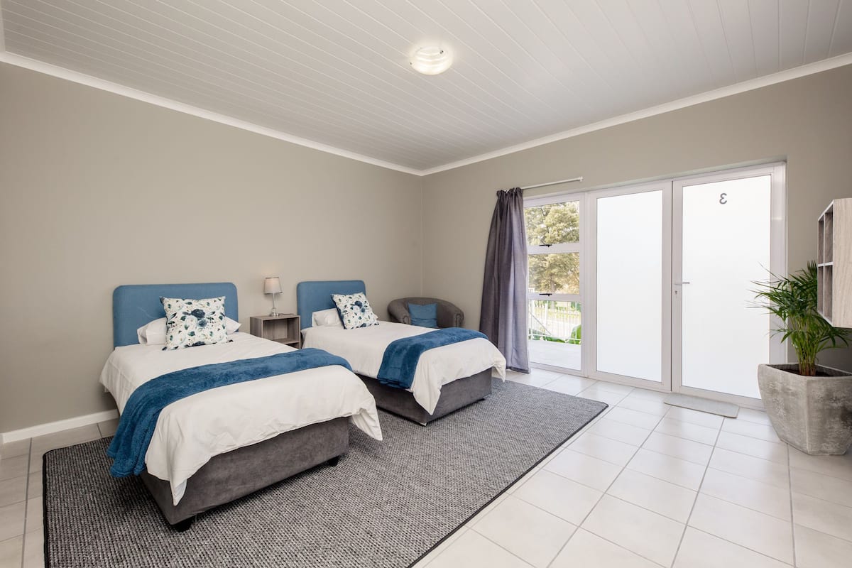 A modern bedroom with two beds, a large window, and a potted plant.