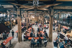 A spacious indoor market with wooden tables and benches, a high ceiling with exposed beams, and a variety of food stalls. - Villa Eika (Grabouw)