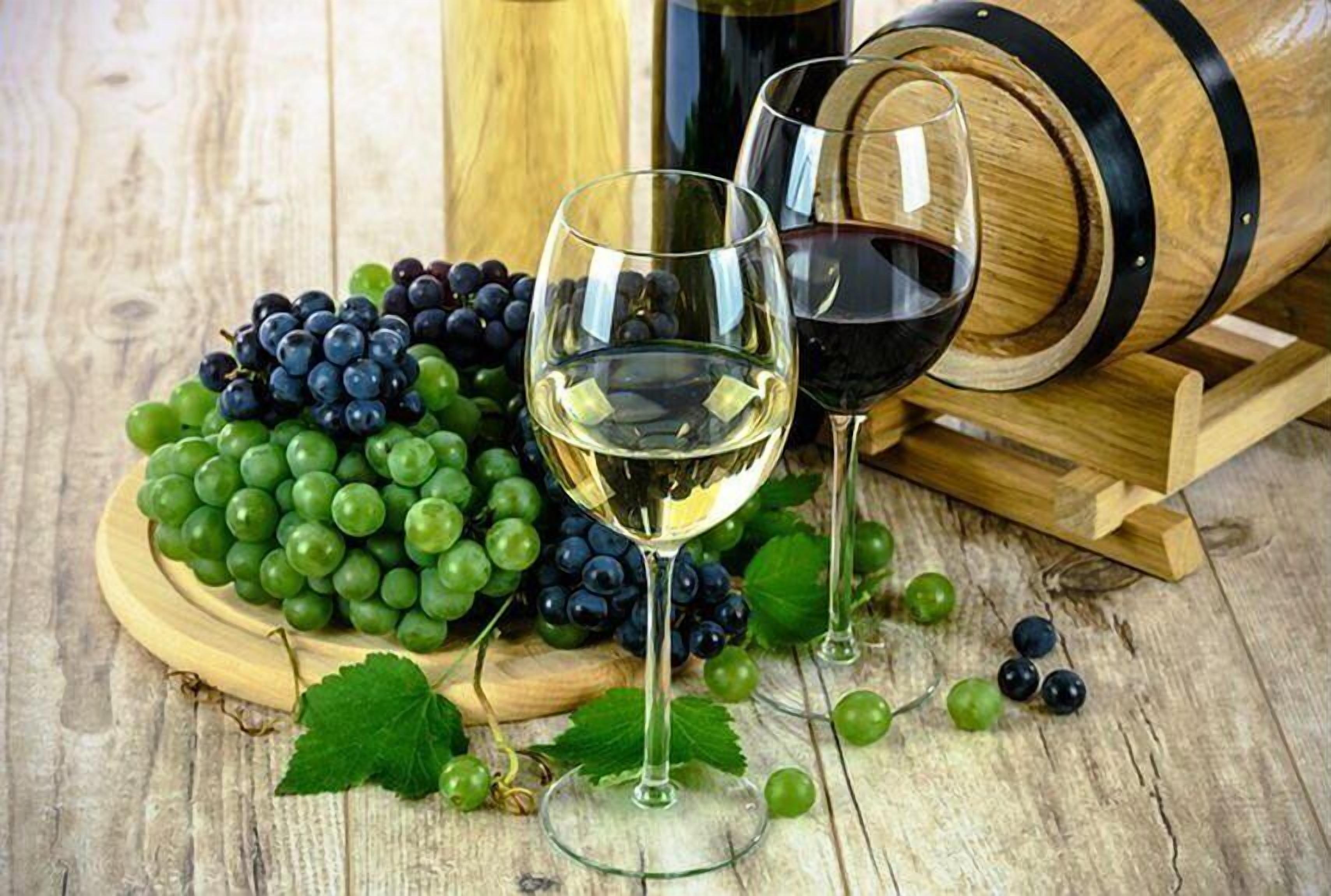 A wooden barrel, two wine glasses, and a wooden board with green and dark grapes.