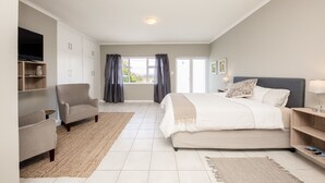 A bedroom with a bed, a chair, a TV, and a window with curtains.