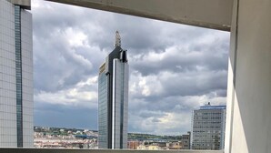 Un balcon avec une table et des chaises, une petite table avec une bougie, et une vue sur un paysage urbain avec de hauts immebles.