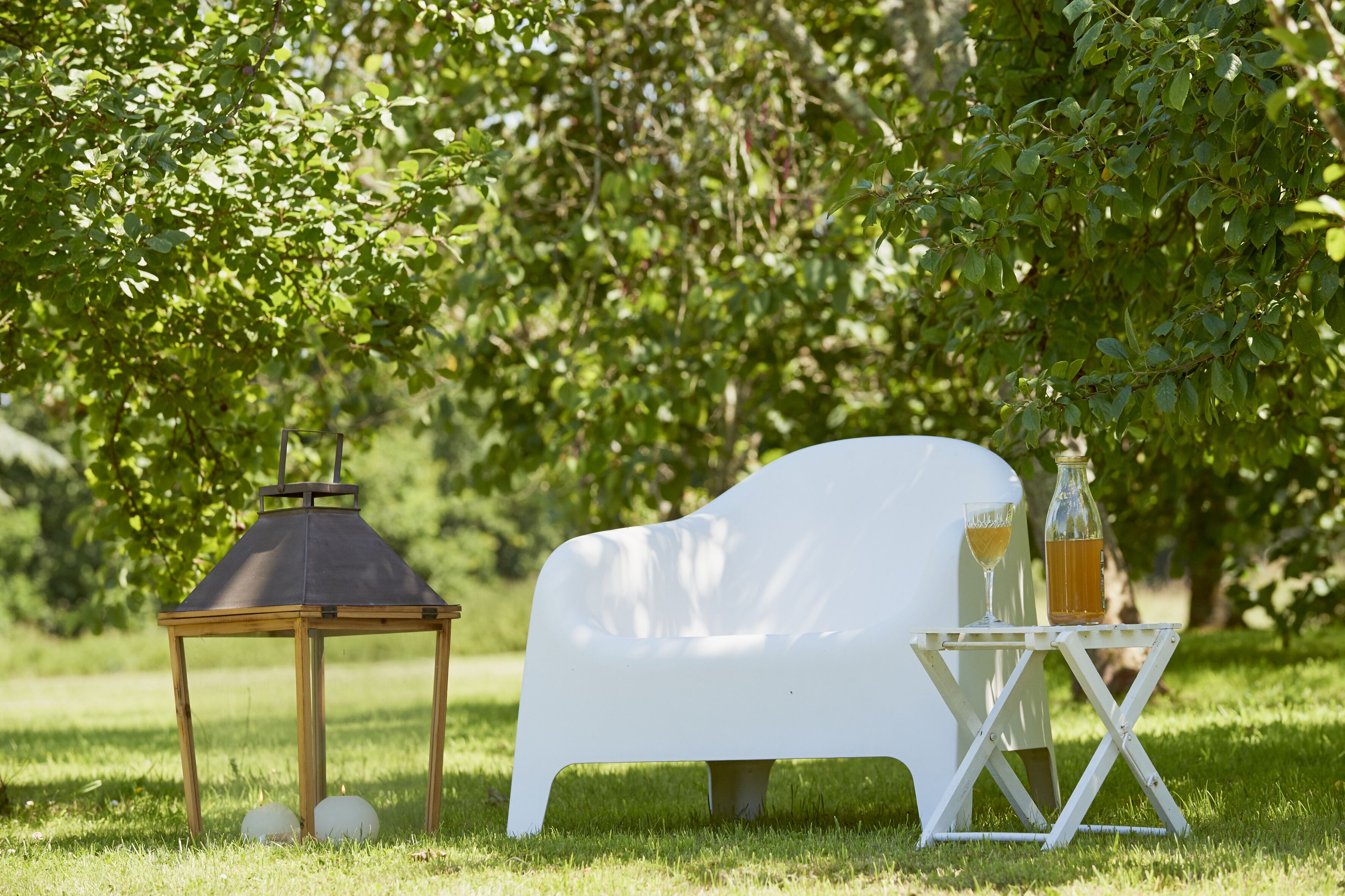 A white outdoor seating area with a table, a lantern, and a bottle of drink.