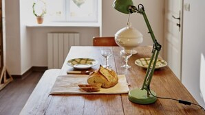 Een houten eettafel met een groene bureaulamp, borden, glazen en een brood.