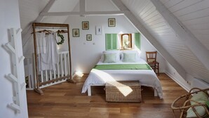 Een slaapkamer met een loft-plafond, een bed met groen beddengoed, een rieten mand en een houten stoel.