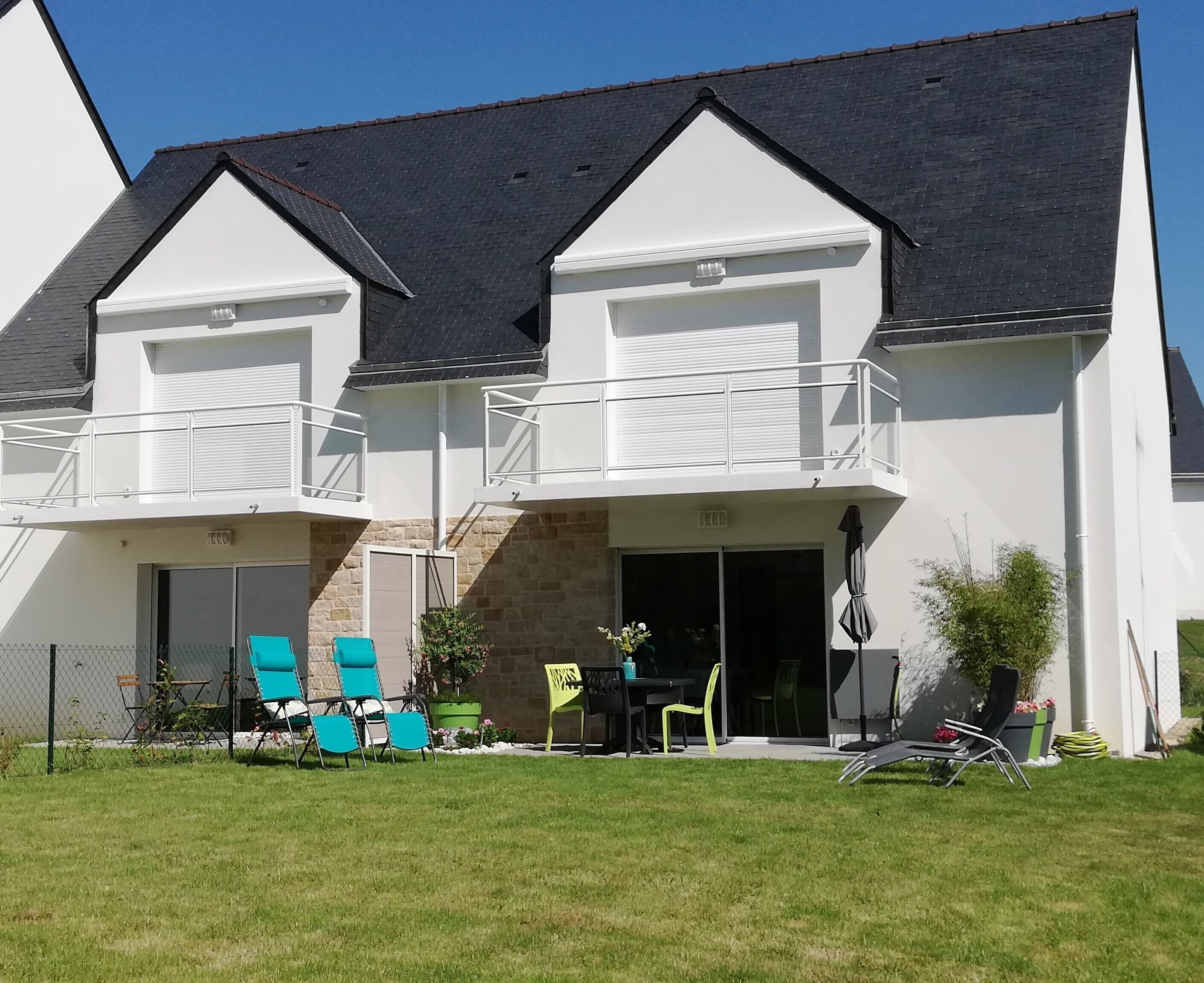 A two-story house with a balcony, a covered patio, and a fenced backyard with outdoor furniture.