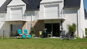 Ein zweistöckiges Haus mit einem Balkon, einer überdachten Terrasse und einem eingezäunten Garten mit Gartenmöbeln.