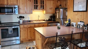 Une cuisine dotée de meubles en bois, d’appareils électroménagers en acier inoxydable, d’une table à manger en bois avec des chaises, et d’un coin repas pour animaux de compagnie.