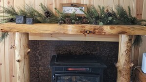 Une cheminée en bois, surmontée d’une étagère décorée de branches de pin et de pommes de pin.