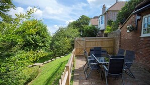 A patio with a table and chairs, a wooden fence, and a brick wall. - The Stables at Boreham House (Hailsham)