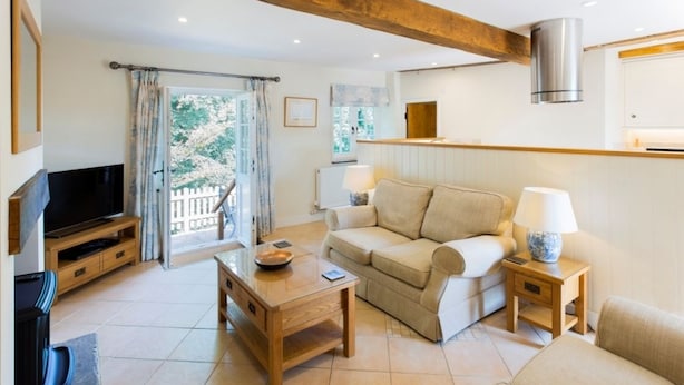A modern living room with a sofa, coffee table, TV, and a balcony with curtains. - The Stables at Boreham House (Hailsham)