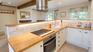 A modern kitchen with white cabinets, a wooden countertop, a built-in oven, and a stainless steel range hood. - The Stables at Boreham House (Hailsham)