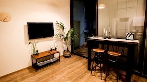 A modern kitchen with a wooden countertop, two stools, a potted plant, and a wall-mounted TV. - CTLV - Tchernikhovski 19 (Tel Aviv)