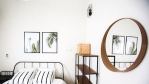 A bedroom with a bed, a wooden shelf with baskets, a round mirror, and two framed pictures on the wall. - CTLV - Tchernikhovski 19 (Tel Aviv)