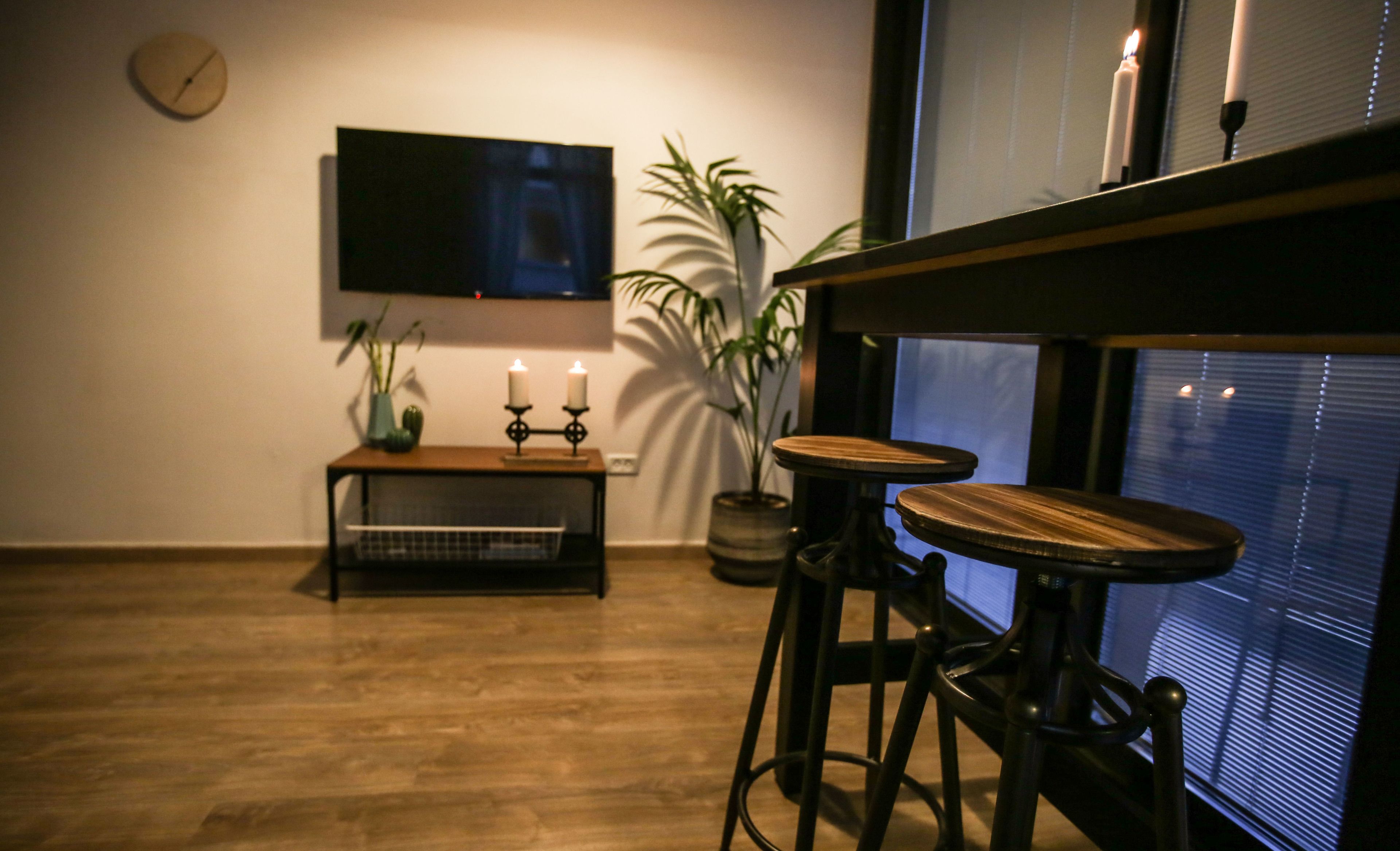 Ein Zimmer mit Holzboden, einem an der Wand montierten Fernseher, einem kleinen Tisch mit Kerzen und zwei Barhocker.