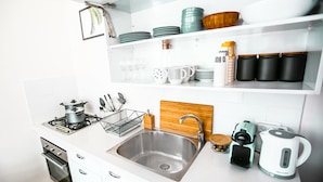 A modern kitchen with white cabinets, a stainless steel sink, a wooden cutting board, a kettle, and various kitchen utensils. - CTLV - Tchernikhovski 19 (Tel Aviv)