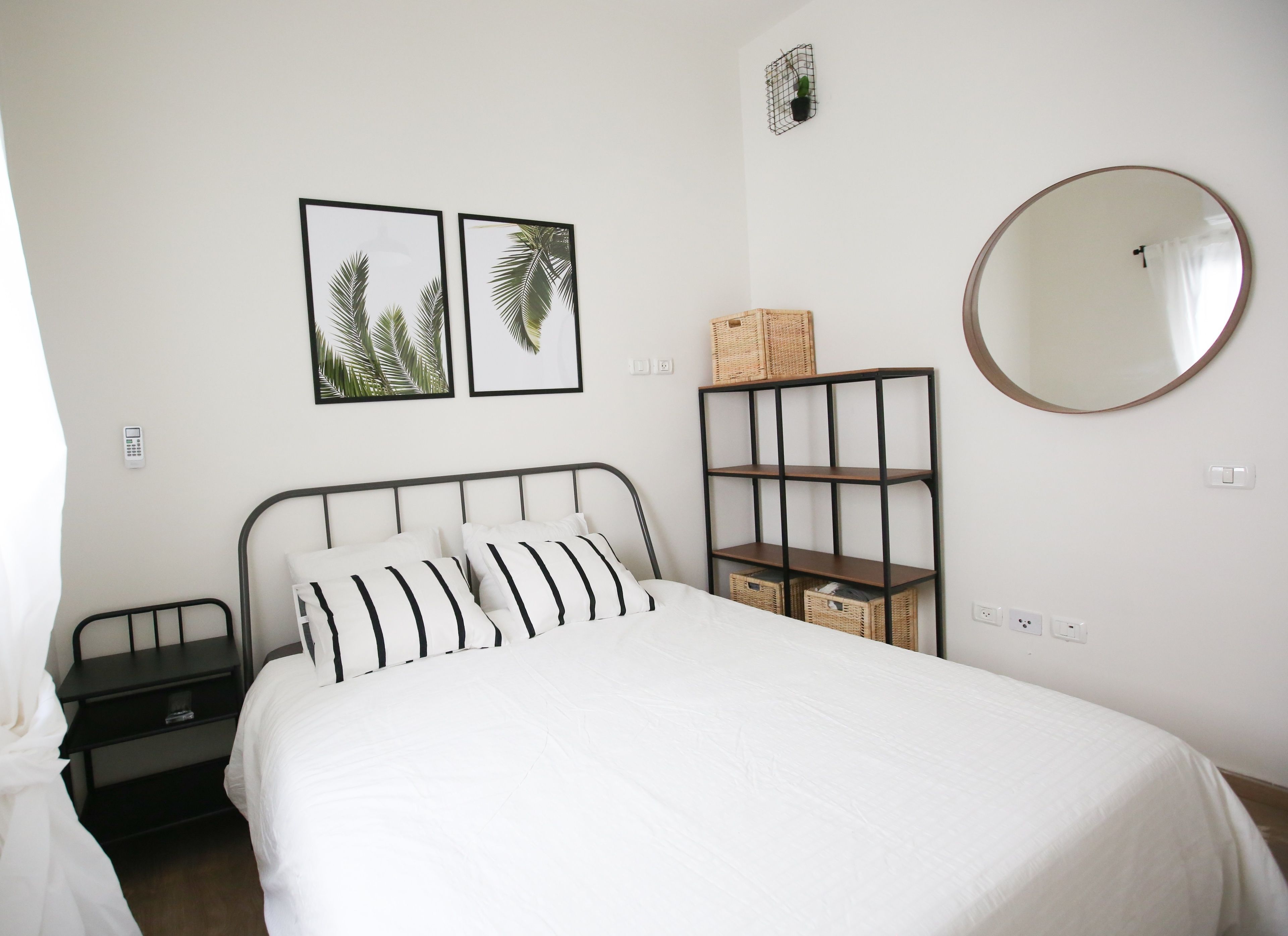 A bedroom with a bed, a bedside table, a wall-mounted shelf, a mirror, and two framed pictures.