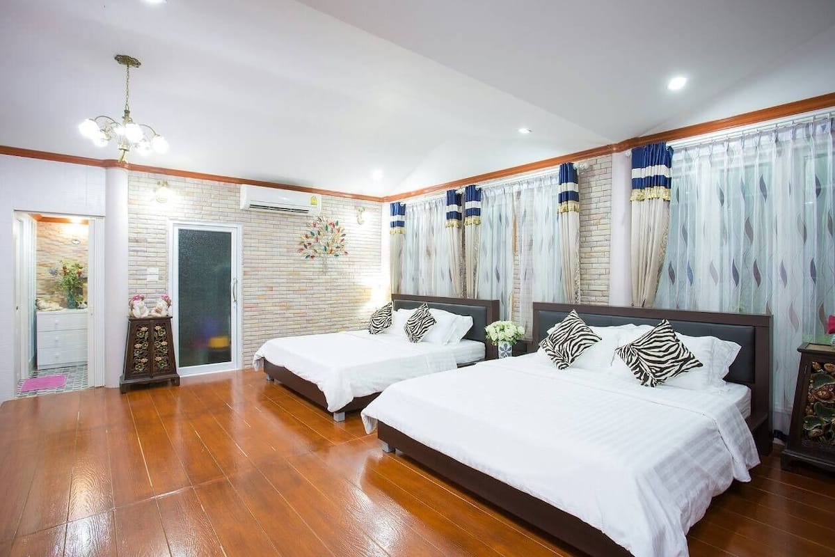 A hotel room with two beds, wooden flooring, a chandelier, and a brick wall.