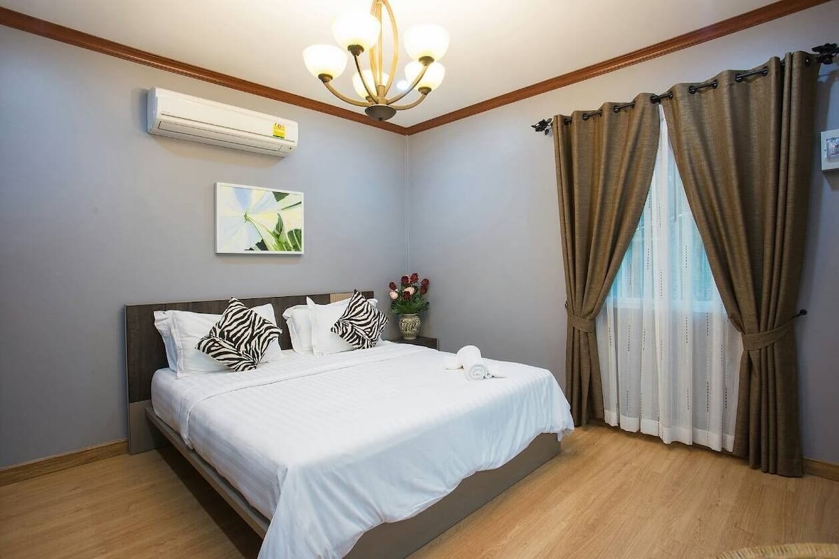 A neatly arranged bedroom with a bed, a ceiling light, an air conditioner, and a window with curtains.