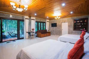 Een moderne hotelkamer met een houten plafond, grote ramen, een bank, een televisie en een bed met rode kussens.