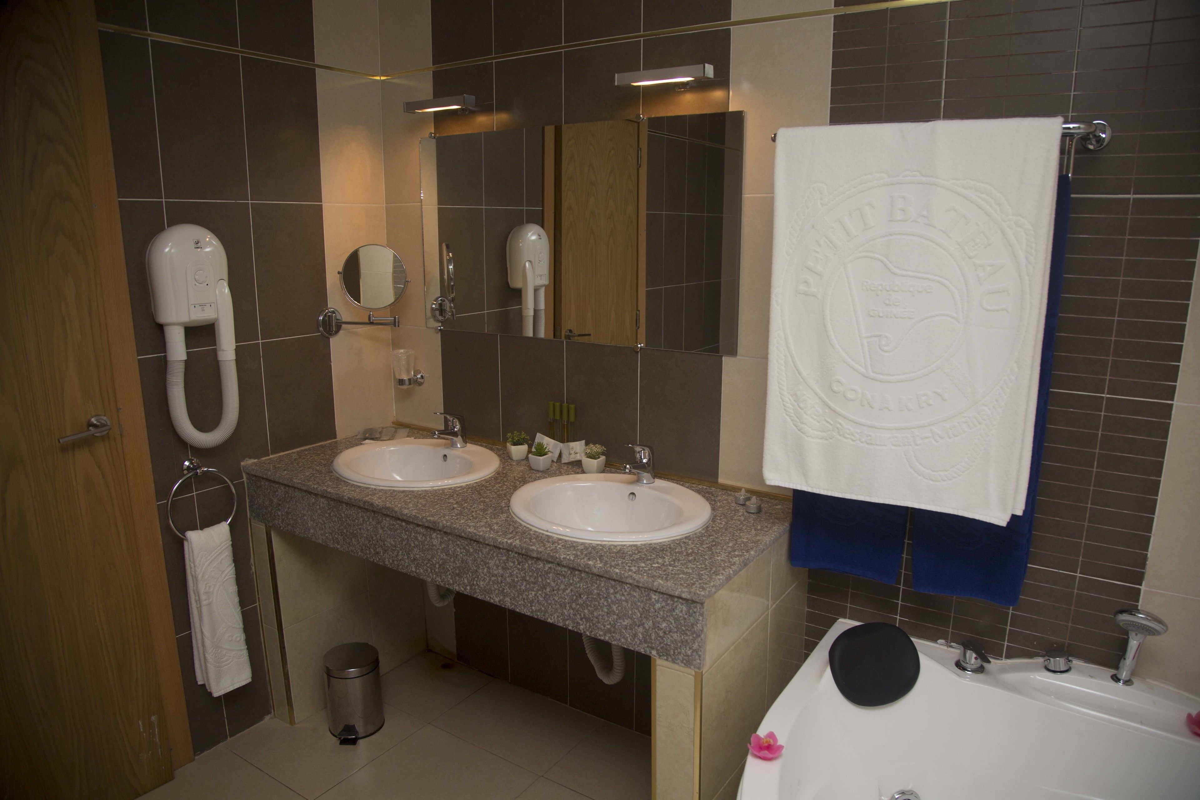A bathroom with two sinks, a mirror, a towel rack, a trash can, and a bathtub.