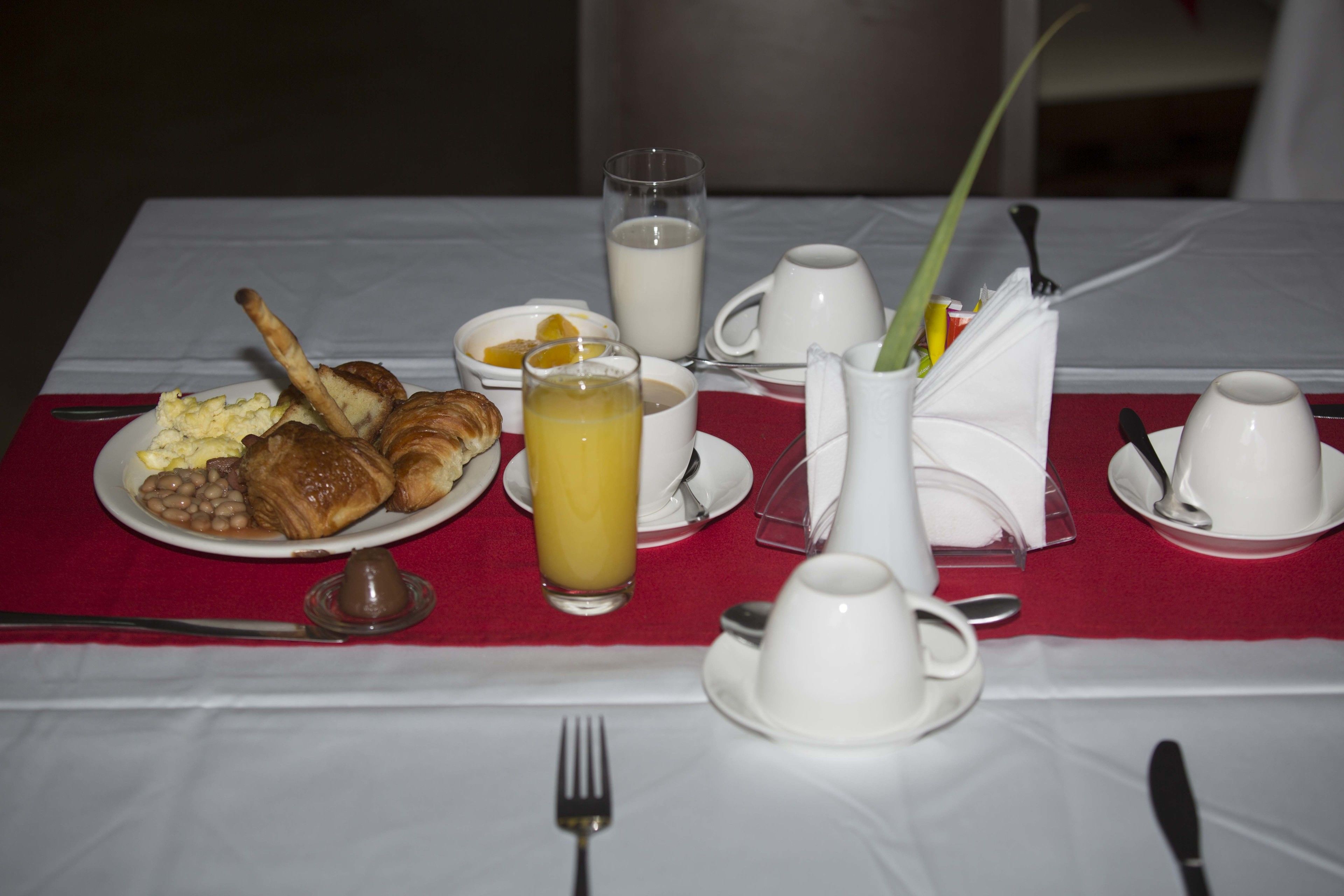 Une table de petit-déjeuner avec des croissants, des haricots, des œufs et un verre de jus d’orange.