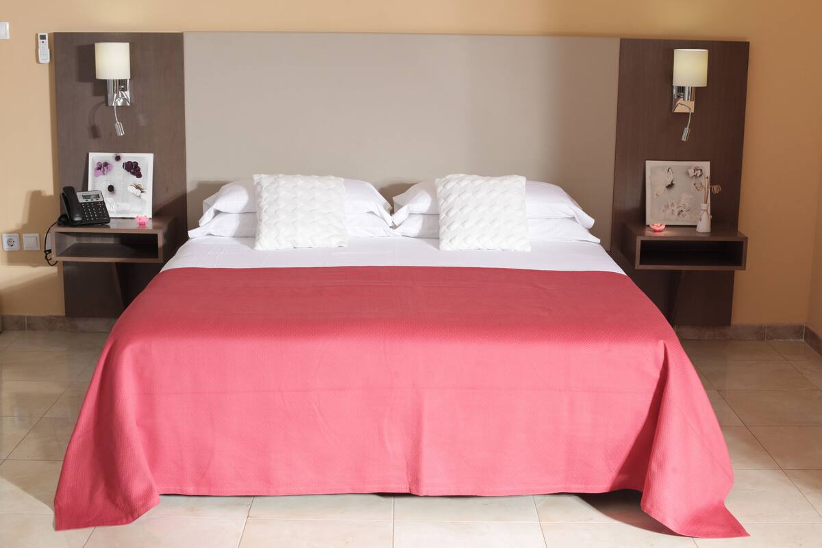 A hotel room with a large bed, two bedside tables, and a red bedspread.