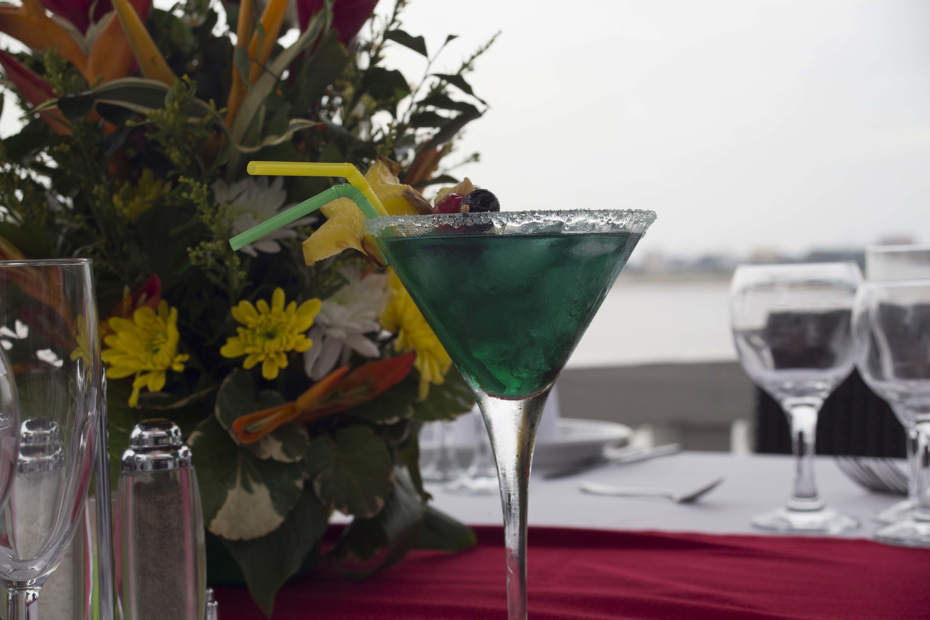 A table with a green cocktail in a martini glass, a clear glass, and a salt shaker.