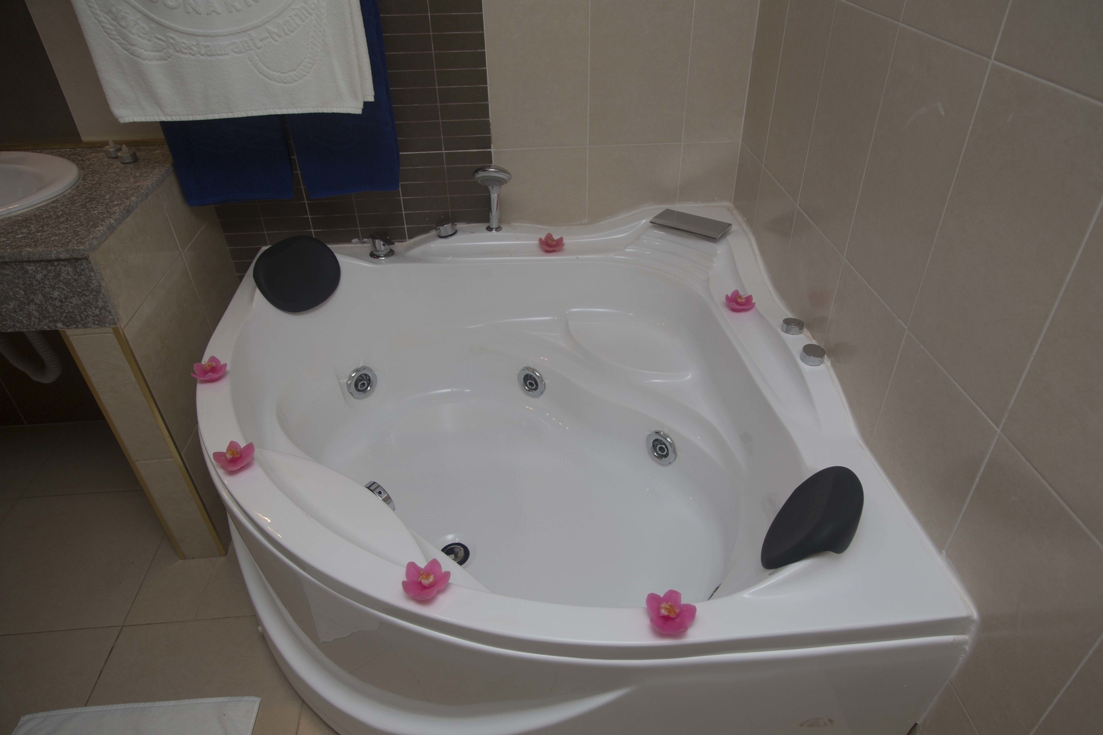 A large, white, freestanding bathtub with multiple faucets and a built-in seat, decorated with pink flowers.