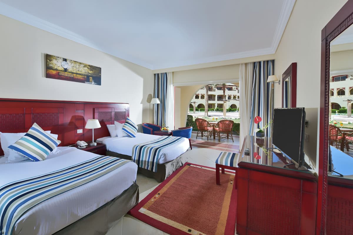 Ein Hotelzimmer mit zwei Betten, einem Fernseher, einem Schreibtisch und einem Balkon mit Blick auf den Hotelinnenhof.
