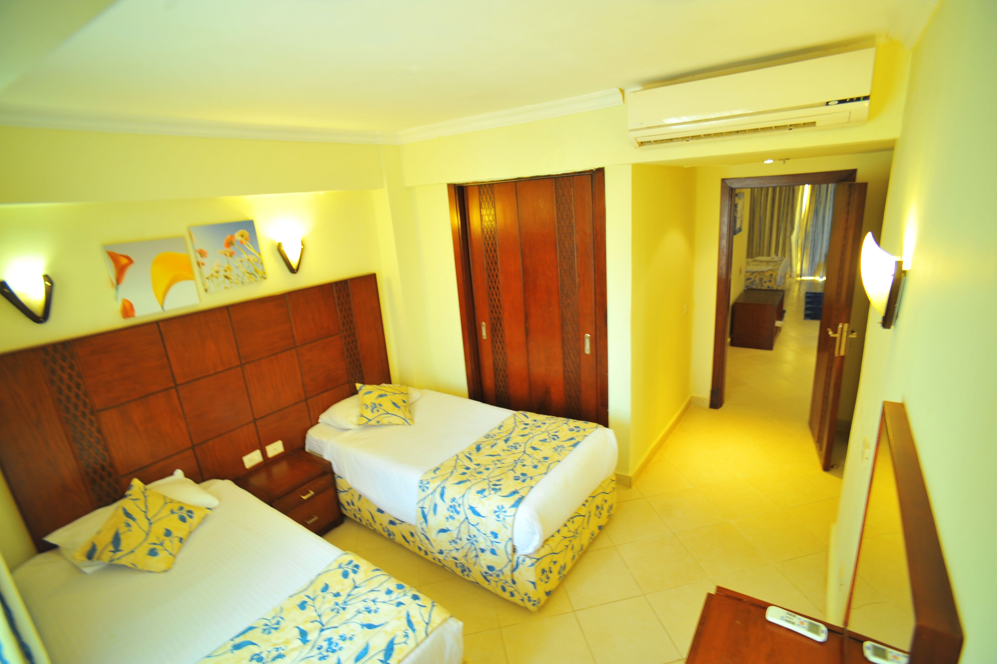 A hotel room with two beds, wooden headboards, and a hallway leading to a bathroom.