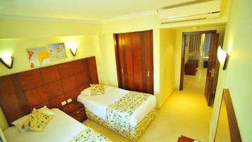 A hotel room with two beds, wooden headboards, and a hallway leading to a bathroom.