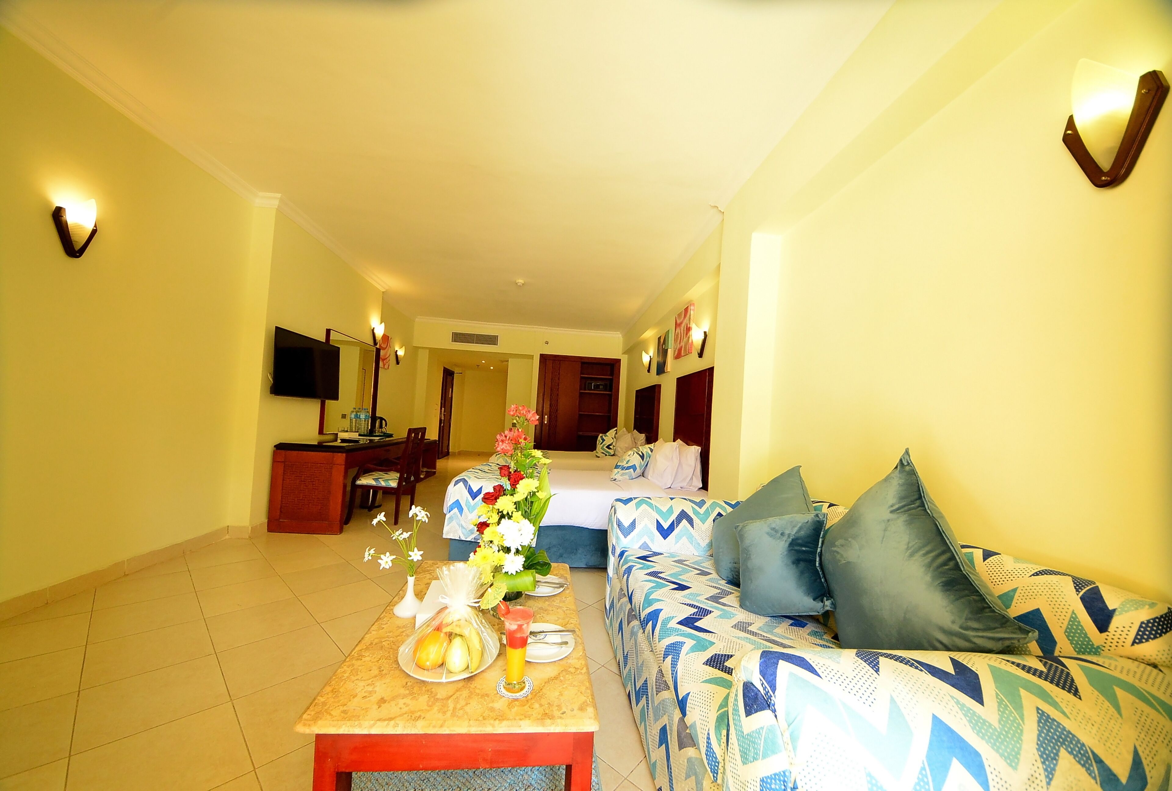 A hotel room with a sofa, a dining table with a vase of flowers, and a television on the wall.