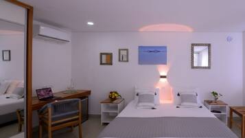 Una habitación de hotel moderna con una cama, mesitas de noche, un escritorio con una computadora portátil, una silla y un espejo grande.
